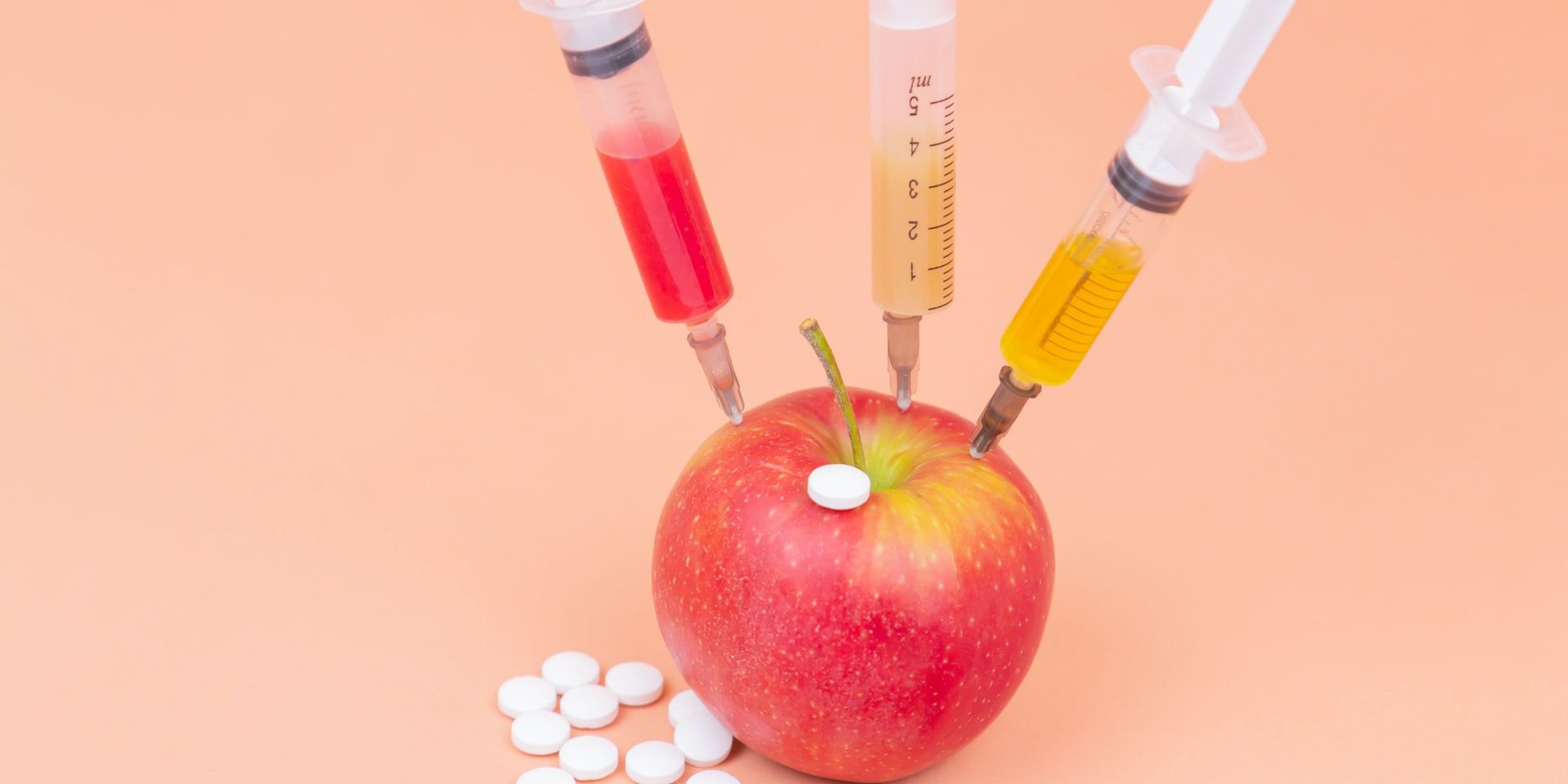 Syringes with different chemicals injections and tablets in a red apple on an orange background