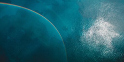 A view of the ocean and a rainbow from above with sunlight reflecting off the water