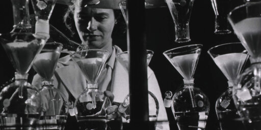 A black and white photo of a person Infront of test tubes