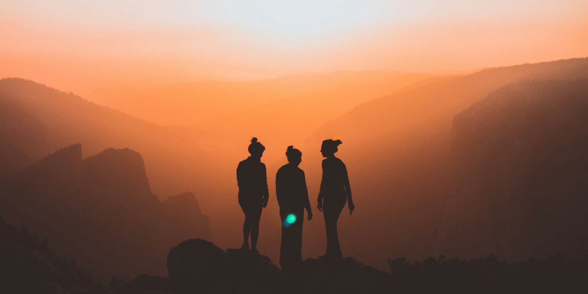 Silhouette of three people on a mountain cliff with sunset in the background