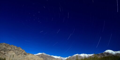 A landscape view of mountains with stars streaking across the clear blue evening sky