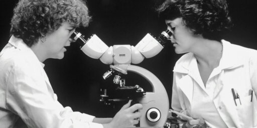 O fotografie alb-negru care arată două femei care se uită într-un microscop