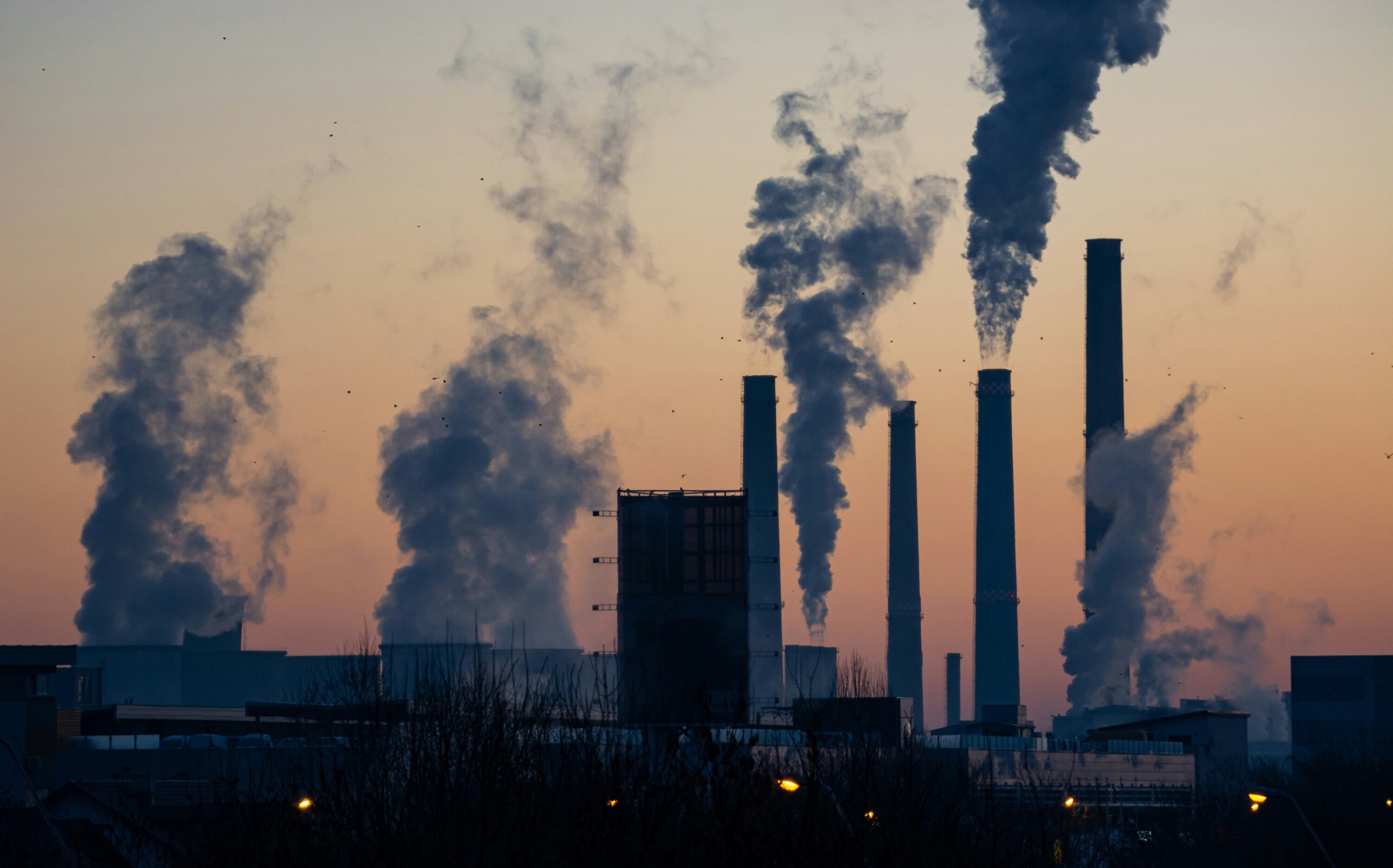 An image of a coal power plant with smoke coming out of the towers during sunset