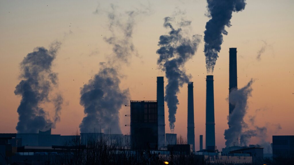 An image of a coal power plant with smoke coming out of the towers during sunset