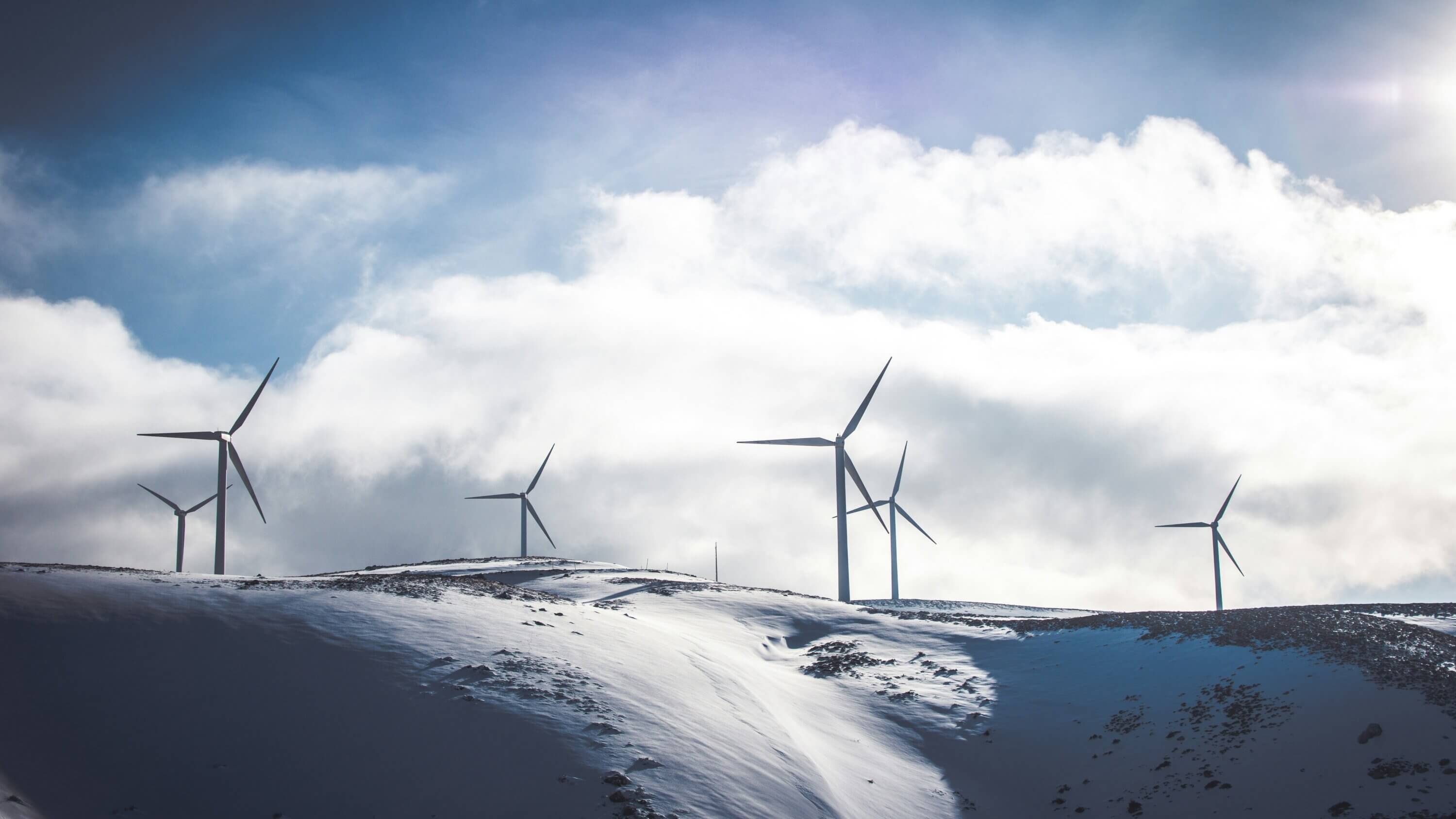 An image of wind turbines in snowy hills with clouds in the background