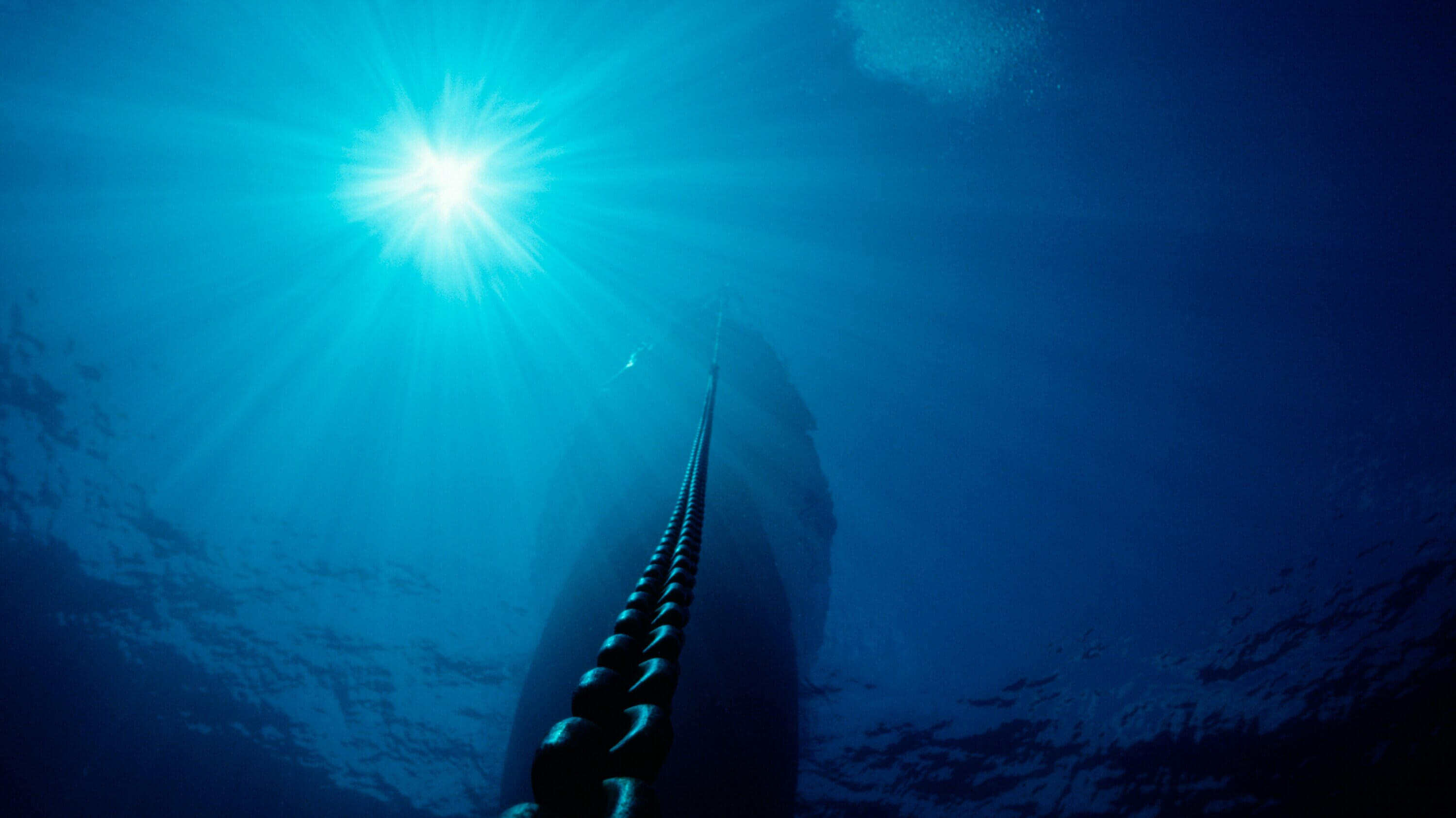 A low angel photo of a ship anchor chain in the sea with the sun shining through the water