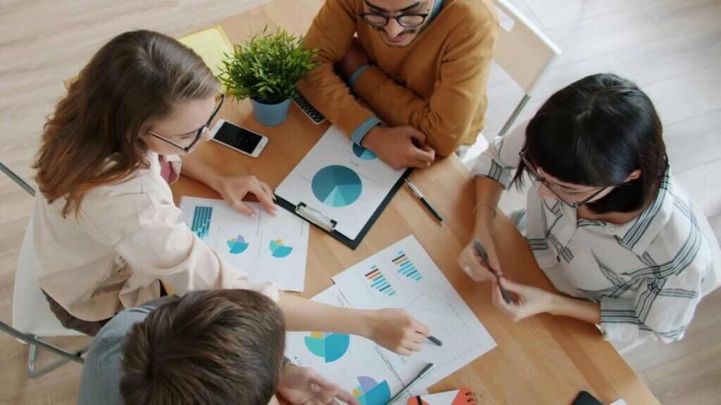 Vista dall'alto di giovani allegri che parlano e lavorano in ufficio, per poi darsi il cinque, godendosi una collaborazione produttiva. Concetto di lavoro, affari ed emozioni.